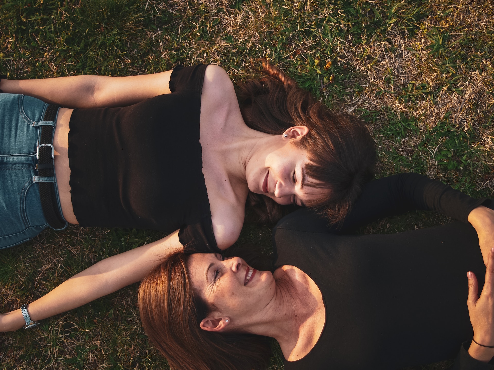 mother and daughter laying on the grass looking at each other saying happy mother's day