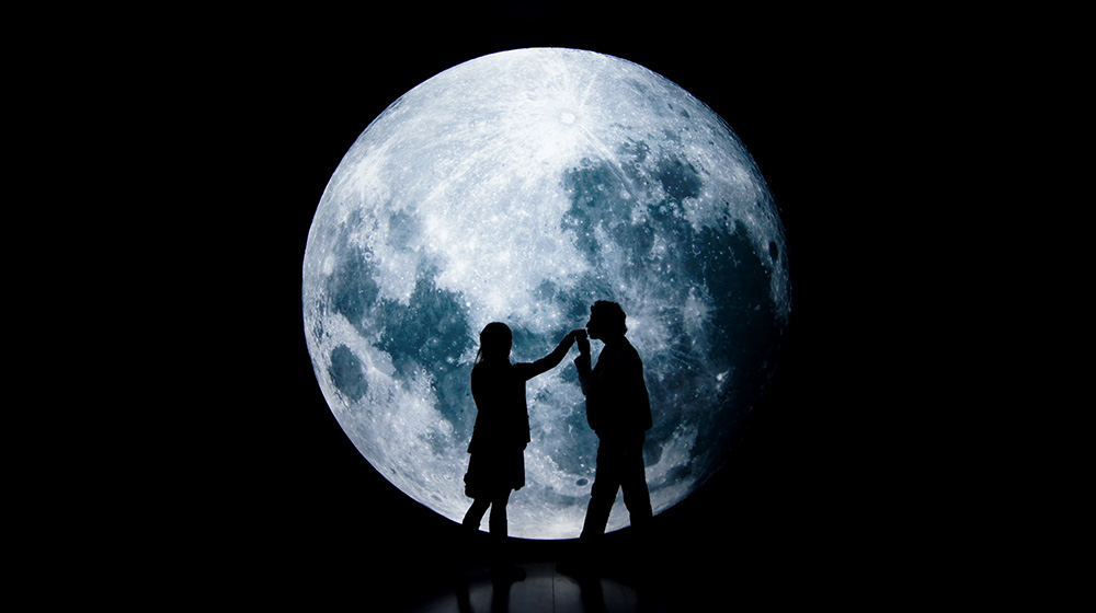 man kissing the hand of women with a giant moon in the background