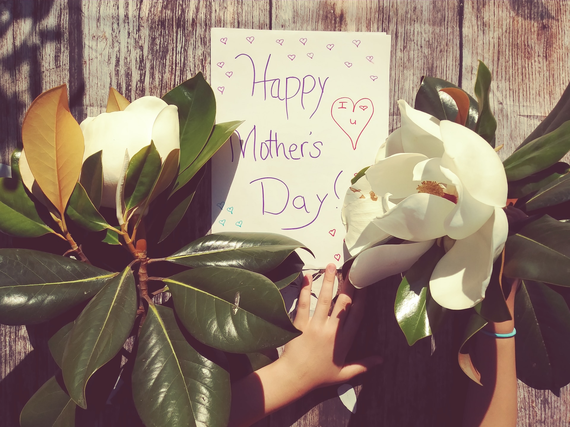 happy mother's day wish in a paper glued in a wooden fence with a children's hand on it