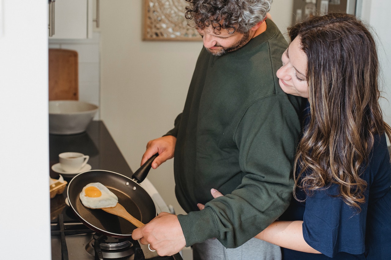 man cooking eggs while wife is hugging and saying good morning for him