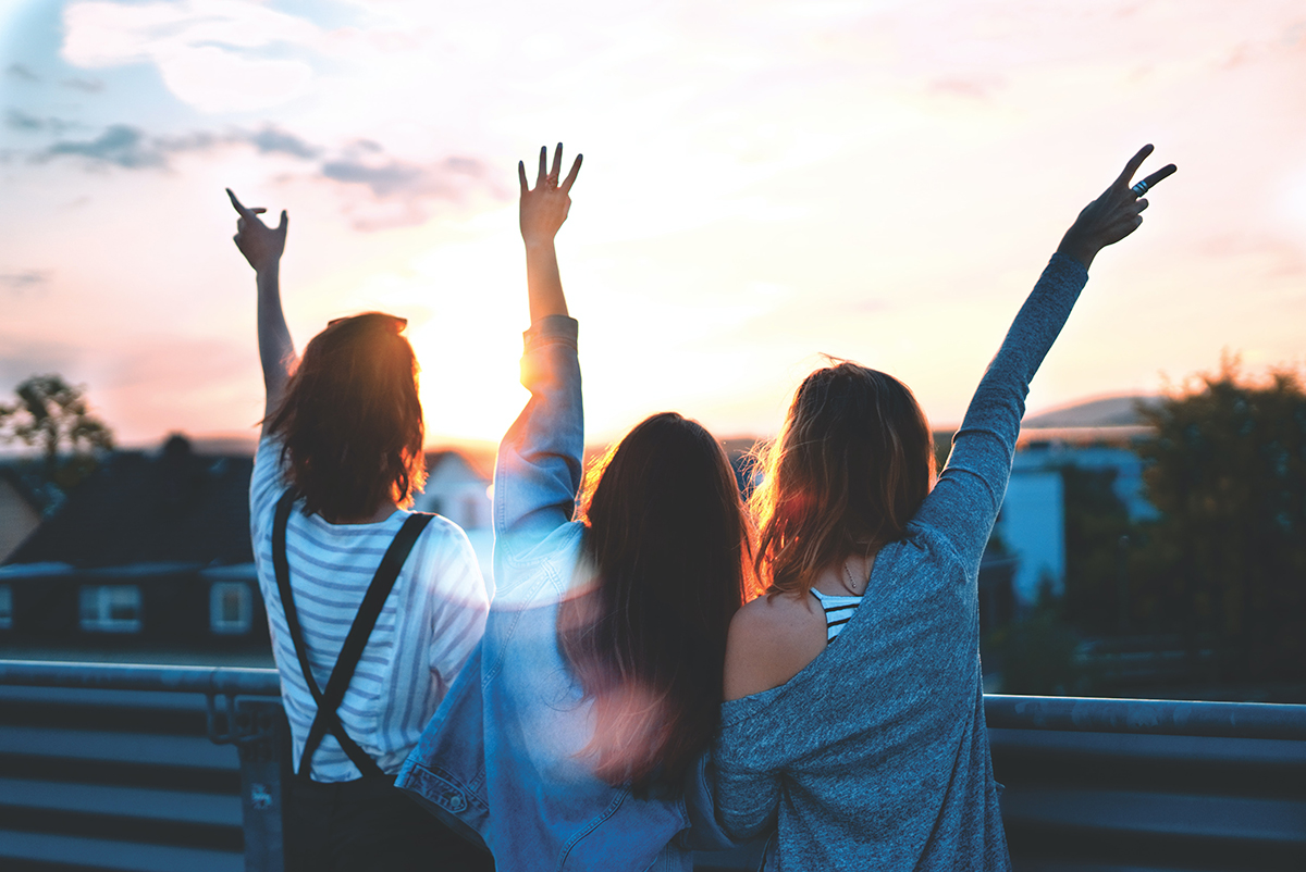 three teenagers having fun together looking at the sunset with raised arms in celebration