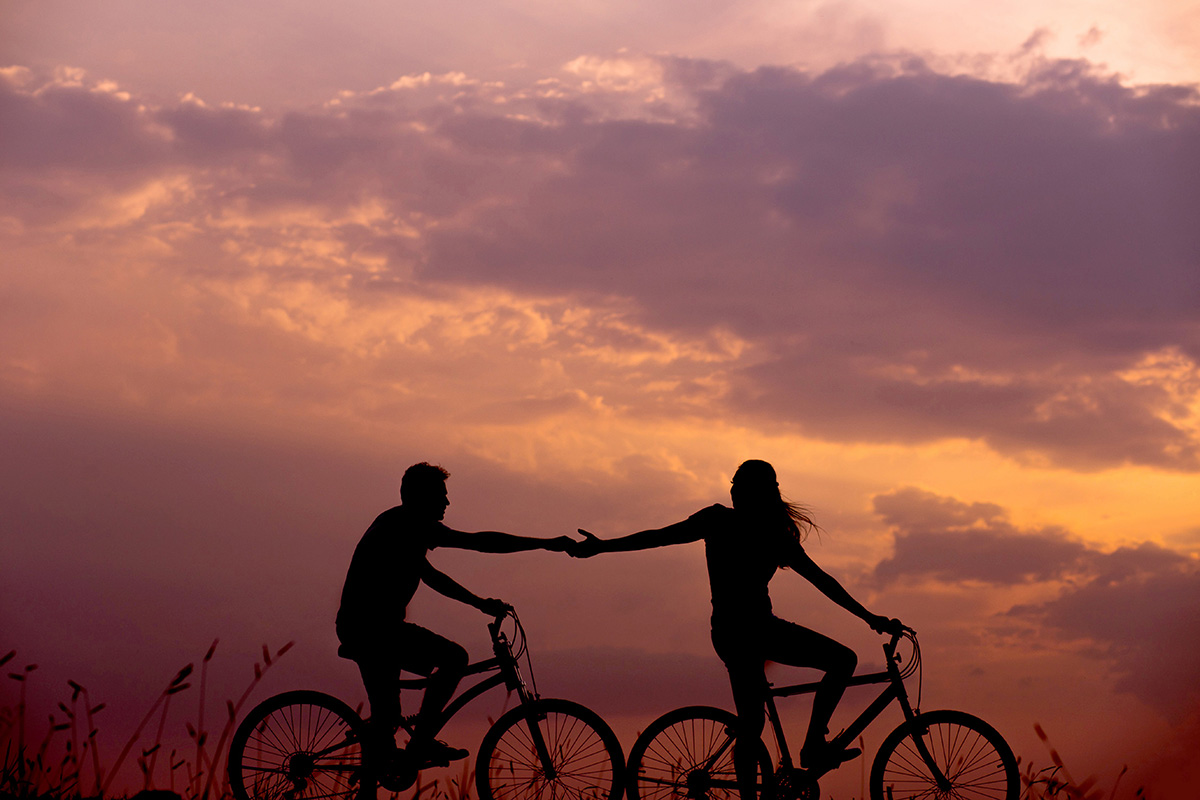 Two people riding bikes in the dusk holding hands in a romantic way