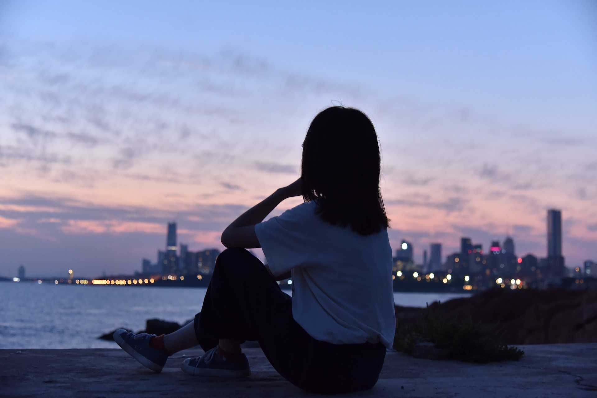 woman sitting at night watching a city skyline missing someone