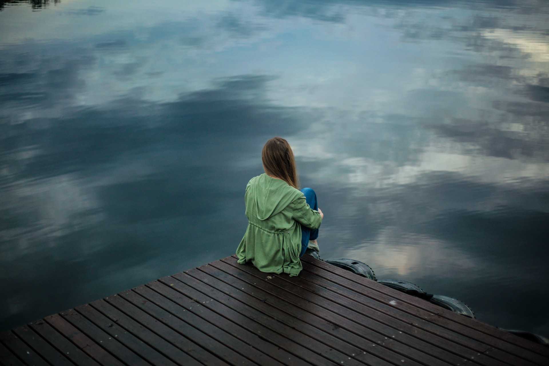 woman sitting in a dock by the lake alone after receiving break up messages for girlfriend