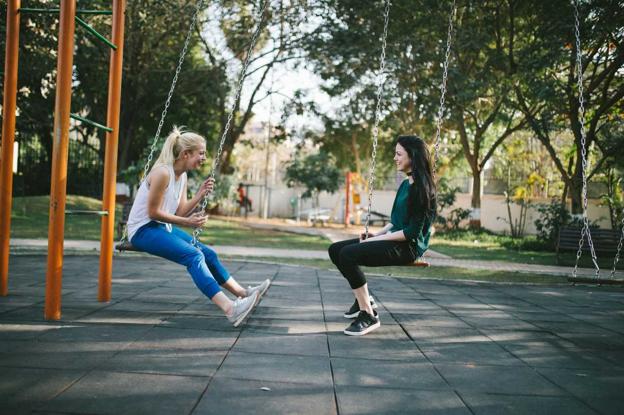 friends laughing and talking seated in swings in a kid's park for Valentine's Day message