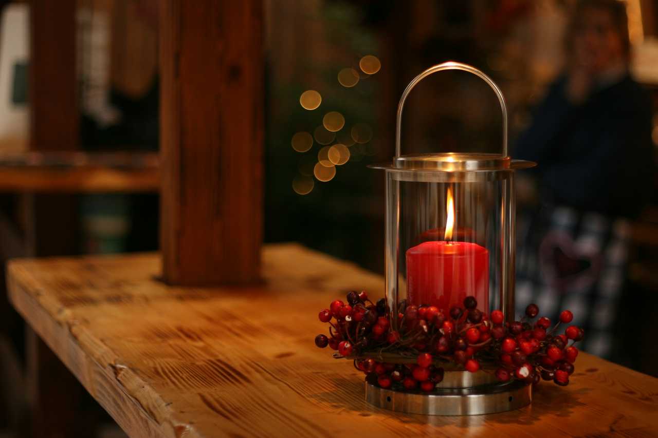 red Christmas candle decorated with flowers inside a glass lamp on a wooden board for Christmas messages and wishes