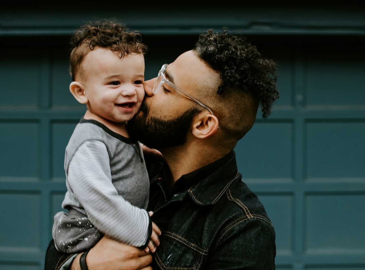 father kissing toddler son in the cheek holding in his arms and smiling for father's day quotes