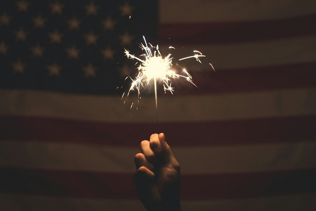 person holding fire sparkler in front of a US flag for independence day messages and quotes