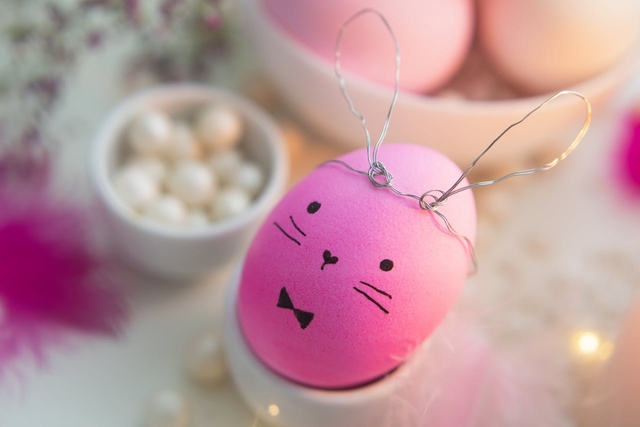 pink egg painted like a bunny in a easter decor setup for happy easter greetings in other languages