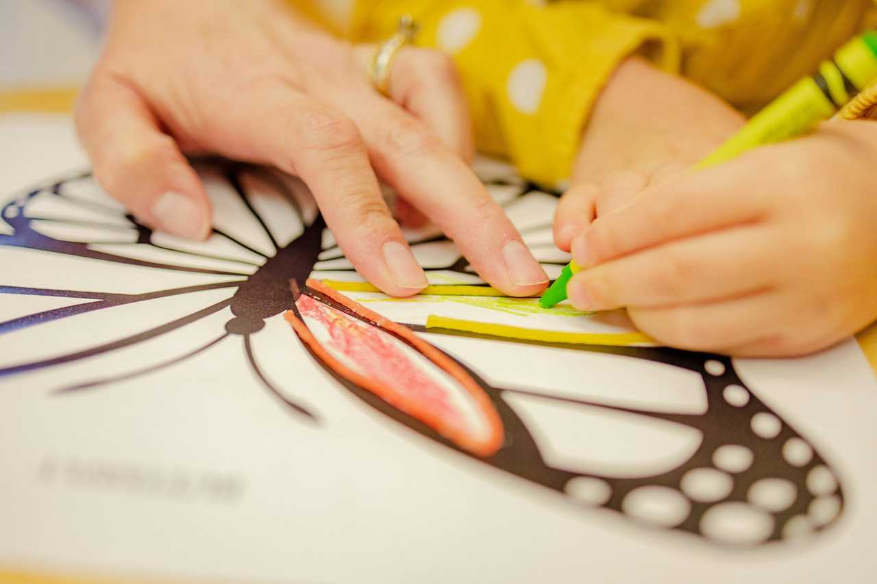 detail of hand of kindergarten teacher and a toddler learning to color 