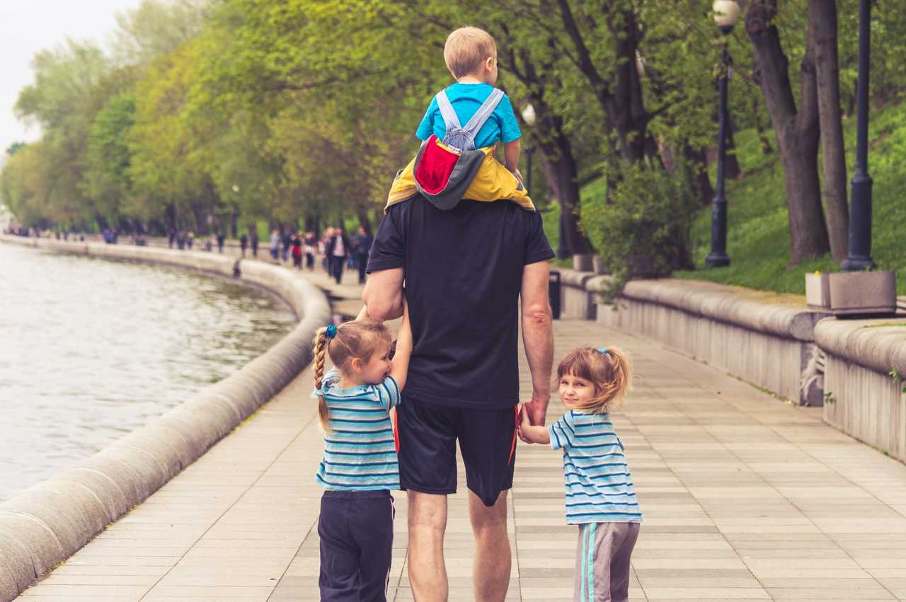 father carrying kid in his shoulders and taking two other daughters by hand