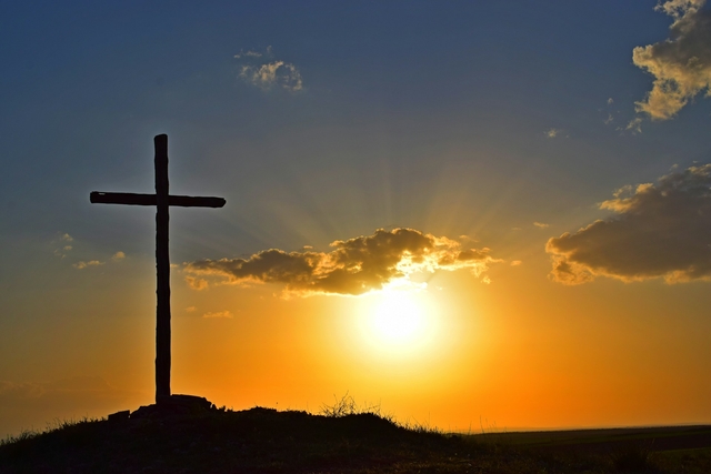 cross on top of a hill in the sunset to send religious happy easter wishes