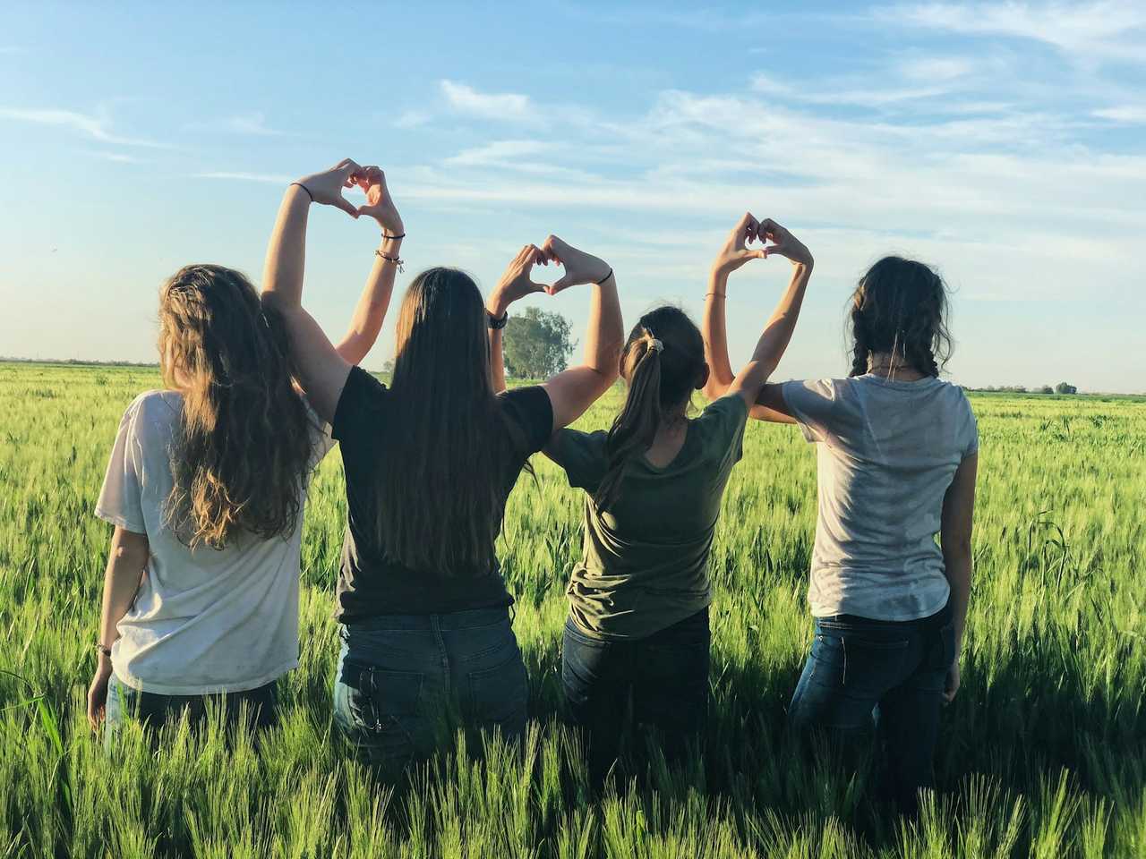 four friends making hearts with their hands in a field