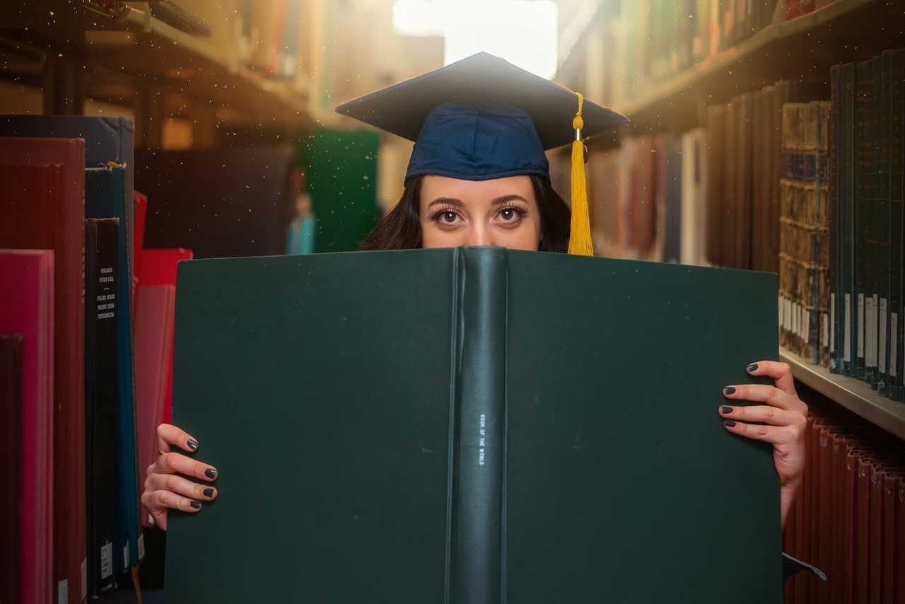 law graduate hiding behind a large law book in a library receiving congratulation messages for her graduation