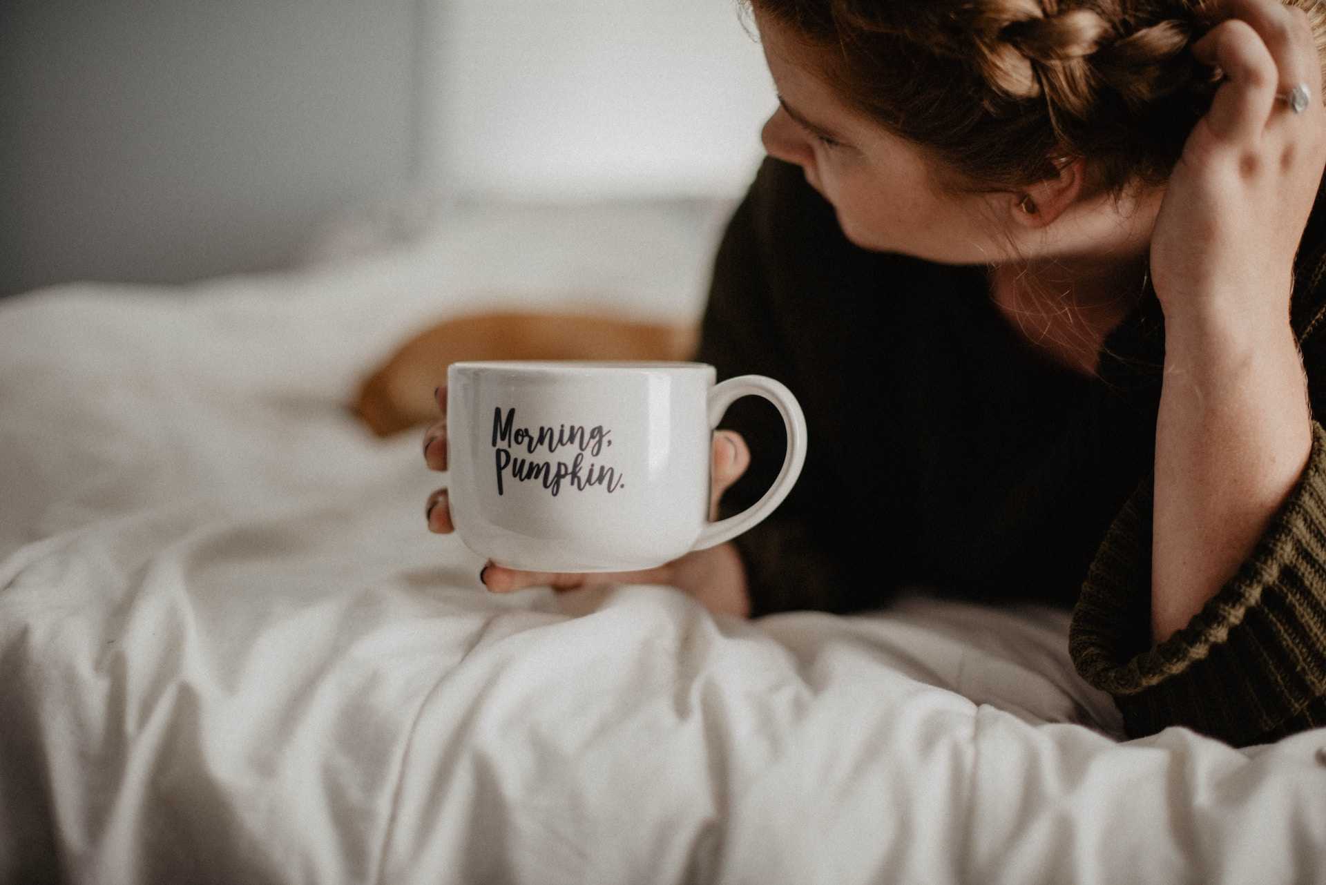 woman laying in bed with cup of coffee after getting good morning wife messages and quotes