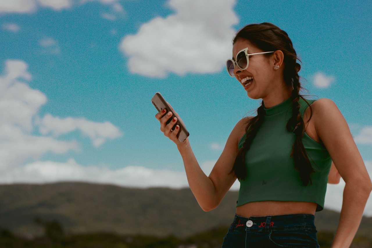 young woman outside with phone in hands and laughing of a e-greeting cards she just received